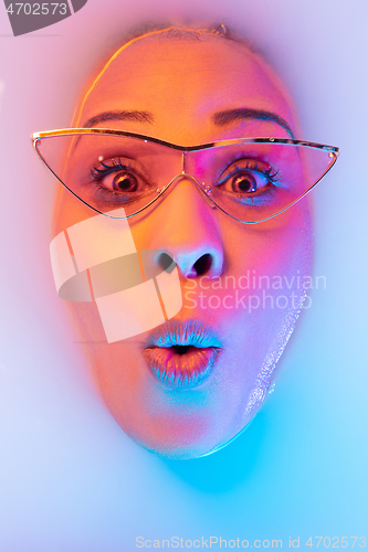 Image of Beautiful female face in the milk bath with soft glowing in blue-pink neon light