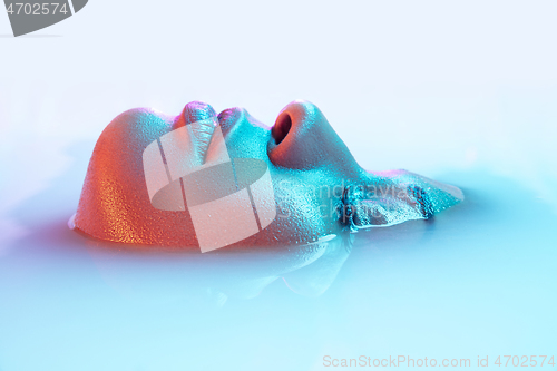 Image of Beautiful female face in the milk bath with soft glowing in blue-pink neon light