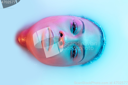 Image of Beautiful female face in the milk bath with soft glowing in blue-pink neon light