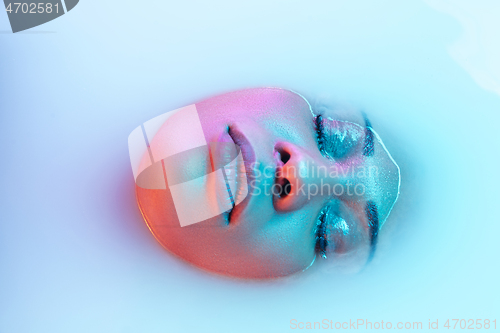 Image of Beautiful female face in the milk bath with soft glowing in blue-pink neon light