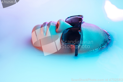 Image of Beautiful female face in the milk bath with soft glowing in blue-pink neon light
