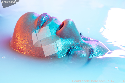 Image of Beautiful female face in the milk bath with soft glowing in blue-pink neon light