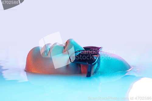 Image of Beautiful female face in the milk bath with soft glowing in blue-pink neon light