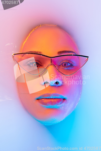 Image of Beautiful female face in the milk bath with soft glowing in blue-pink neon light