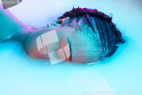 Image of Beautiful female face in the milk bath with soft glowing in blue-pink neon light