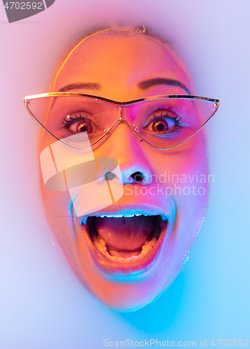 Image of Beautiful female face in the milk bath with soft glowing in blue-pink neon light