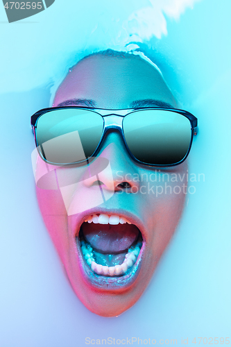 Image of Beautiful female face in the milk bath with soft glowing in blue-pink neon light