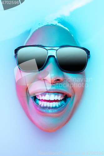 Image of Beautiful female face in the milk bath with soft glowing in blue-pink neon light