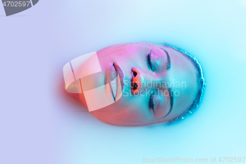 Image of Beautiful female face in the milk bath with soft glowing in blue-pink neon light