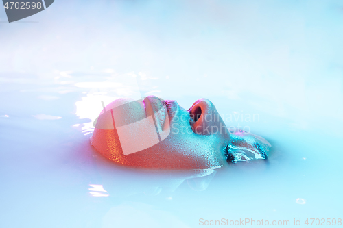 Image of Beautiful female face in the milk bath with soft glowing in blue-pink neon light