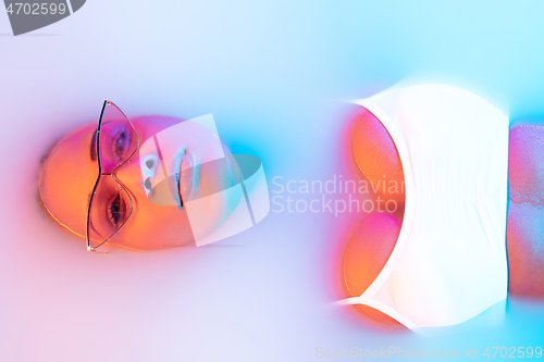 Image of Beautiful female face in the milk bath with soft glowing in blue-pink neon light