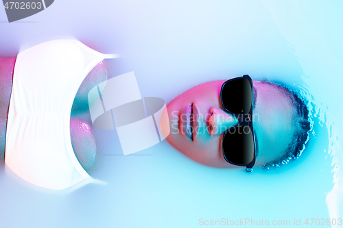 Image of Beautiful female face in the milk bath with soft glowing in blue-pink neon light