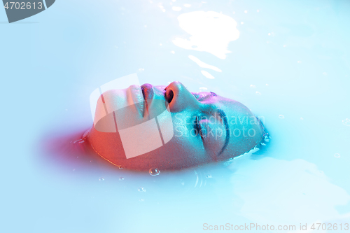 Image of Beautiful female face in the milk bath with soft glowing in blue-pink neon light