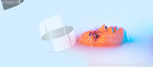 Image of Beautiful female face in the milk bath with soft glowing in blue-pink neon light