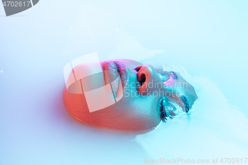 Image of Beautiful female face in the milk bath with soft glowing in blue-pink neon light