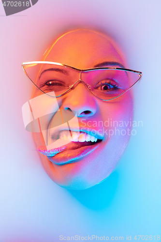 Image of Beautiful female face in the milk bath with soft glowing in blue-pink neon light