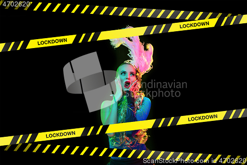 Image of Beautiful young woman in carnival, stylish masquerade costume with feathers behind limiting tapes with word Lockdown