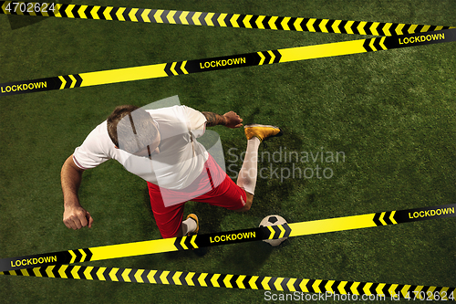 Image of Football or soccer player on grass background behind limiting tapes with word Lockdown