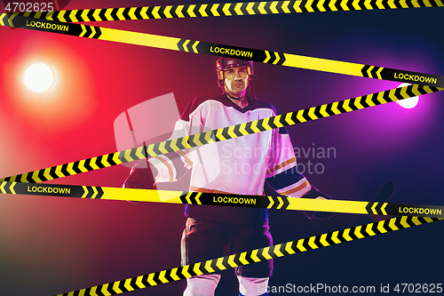 Image of Male hockey player wearing equipment, helmet posing on gradient background behind limiting tapes with word Lockdown