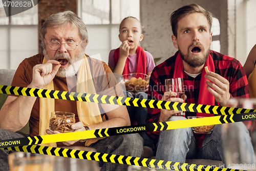 Image of Female and male soccer fans cheering for favourite sport team in restaurant or home behind the limiting tapes with Lockdown