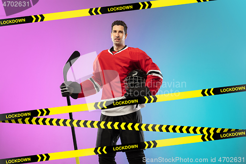 Image of Male hockey player wearing equipment, helmet posing on gradient background behind limiting tapes with word Lockdown