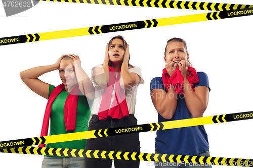 Image of Excited, shocked female soccer fans cheering for favourite sport team isolated on white background with limiting tapes with word Lockdown