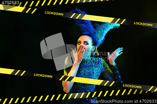 Image of Beautiful young woman in carnival, stylish masquerade costume with feathers behind limiting tapes with word Lockdown