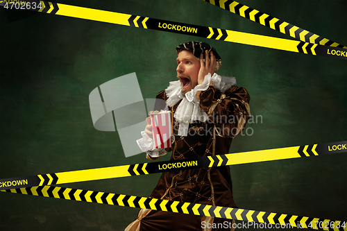 Image of Medieval young man in old-fashioned costume with popcorn behing the limiting tapes with word Lockdown