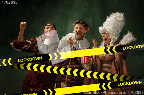 Image of Medieval young man and women in old-fashioned costume with popcorn behing the limiting tapes with word Lockdown