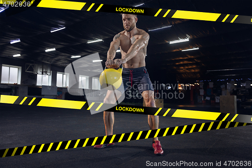 Image of Young sportive man training on gym background behind limiting tapes with word Lockdown
