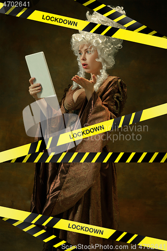 Image of Medieval young woman in old-fashioned costume with tablet behing the limiting tapes with word Lockdown