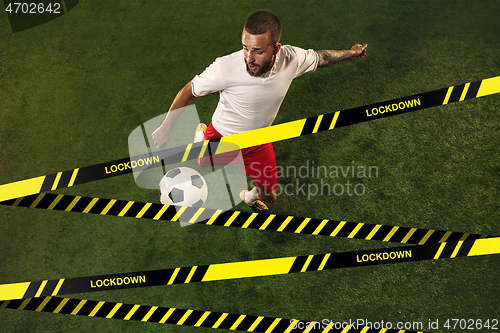 Image of Football or soccer player on grass background behind limiting tapes with word Lockdown