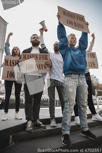 Image of Group of activists protesting, supporting masks for 100 days in America. Look angry, hopeful, confident. Banners and smoke. Coronavirus.