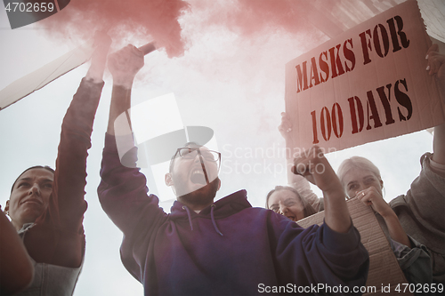 Image of Group of activists protesting, supporting masks for 100 days in America. Look angry, hopeful, confident. Banners and smoke. Coronavirus.