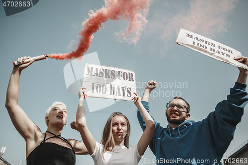 Image of Group of activists protesting, supporting masks for 100 days in America. Look angry, hopeful, confident. Banners and smoke. Coronavirus.