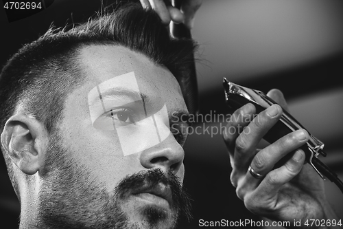 Image of Young handsome barber making haircut for attractive man in barbershop