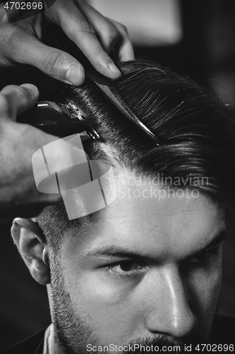 Image of Young handsome barber making haircut for attractive man in barbershop