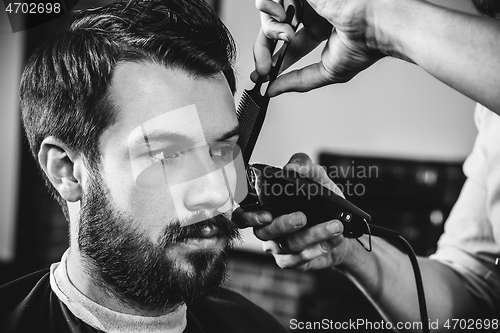 Image of Young handsome barber making haircut for attractive man in barbershop