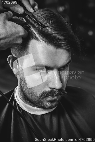 Image of Young handsome barber making haircut for attractive man in barbershop