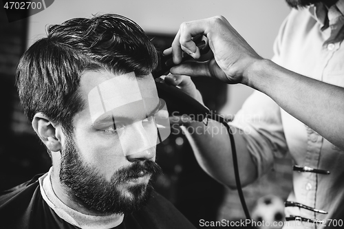 Image of Young handsome barber making haircut for attractive man in barbershop