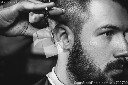 Image of Young handsome barber making haircut for attractive man in barbershop