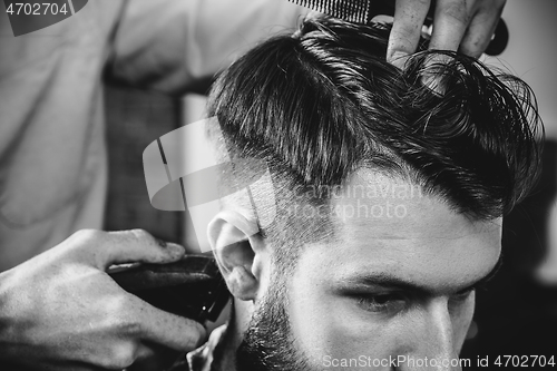 Image of Young handsome barber making haircut for attractive man in barbershop