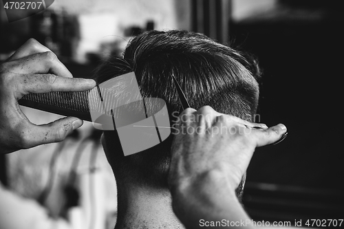 Image of Young handsome barber making haircut for attractive man in barbershop