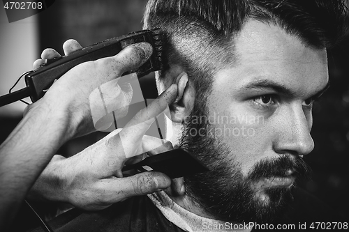 Image of Young handsome barber making haircut for attractive man in barbershop