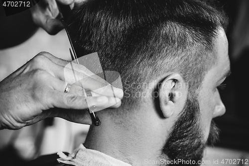 Image of Young handsome barber making haircut for attractive man in barbershop