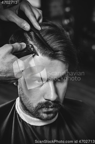 Image of Young handsome barber making haircut for attractive man in barbershop