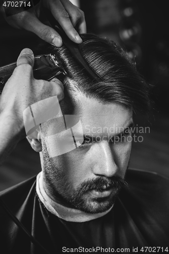 Image of Young handsome barber making haircut for attractive man in barbershop