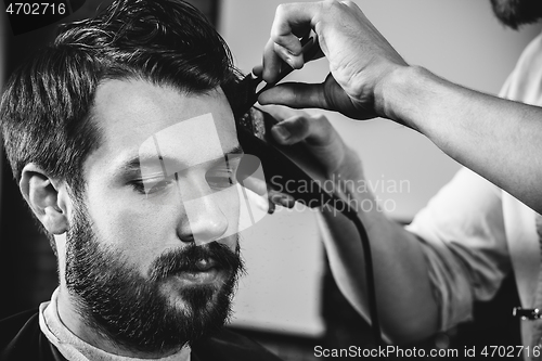 Image of Young handsome barber making haircut for attractive man in barbershop