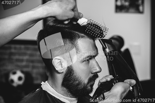 Image of Young handsome barber making haircut for attractive man in barbershop