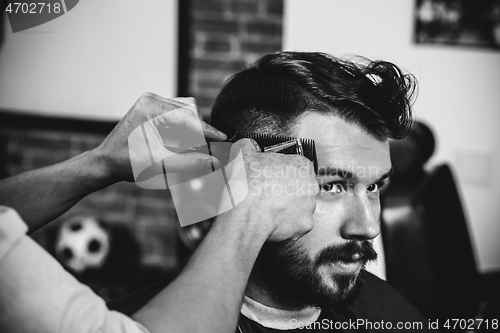 Image of Young handsome barber making haircut for attractive man in barbershop